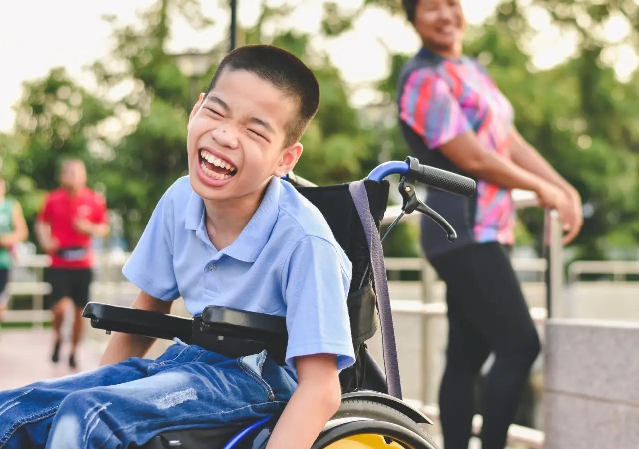 Asian child in wheelchair outside with a big smile on his face